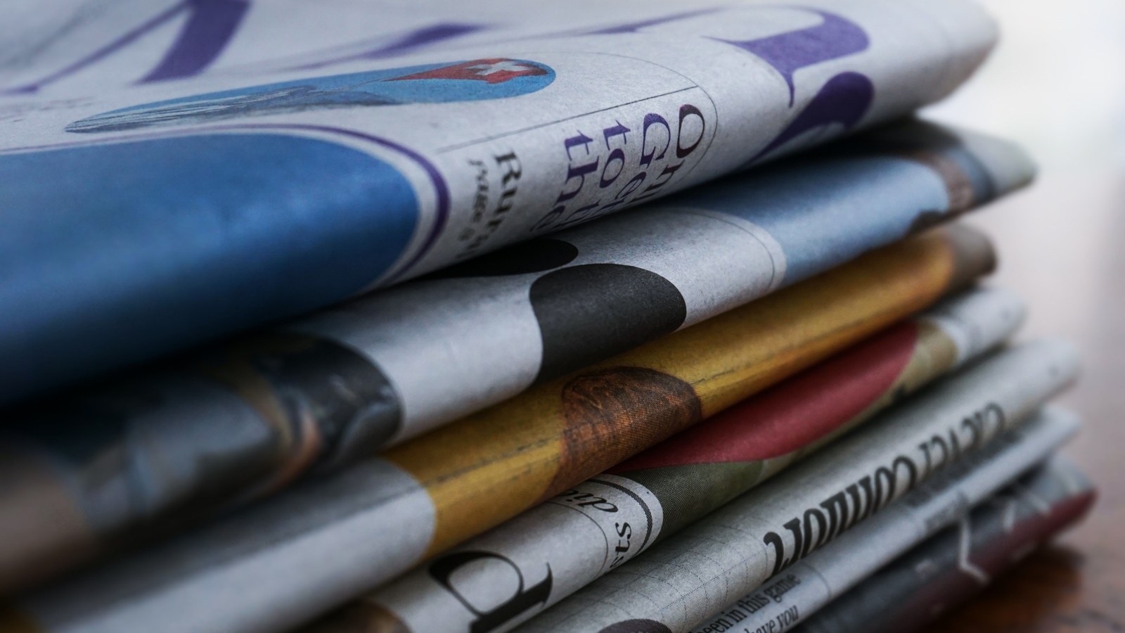 A stack of printed newspapers resting on a wooden table.